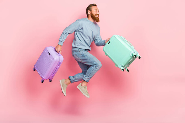 Full size profile portrait of active handsome guy hold suitcases jump run isolated on pink color background. - Foto, immagini