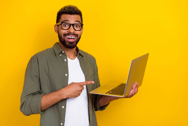Photo of smart excited man wear khaki shirt hand spectacles pointing modern device empty space isolated yellow color background. - 写真・画像