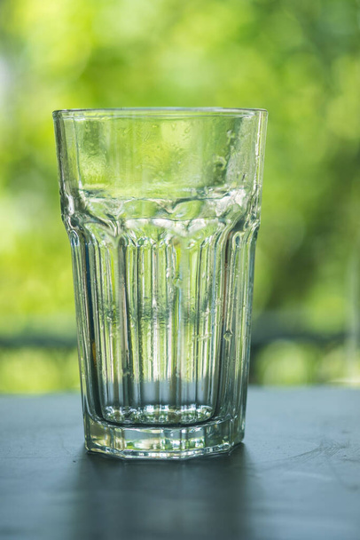 Огранённый стакан воды. Прозрачное стекло на фоне природного размытия. Закрыть - Фото, изображение