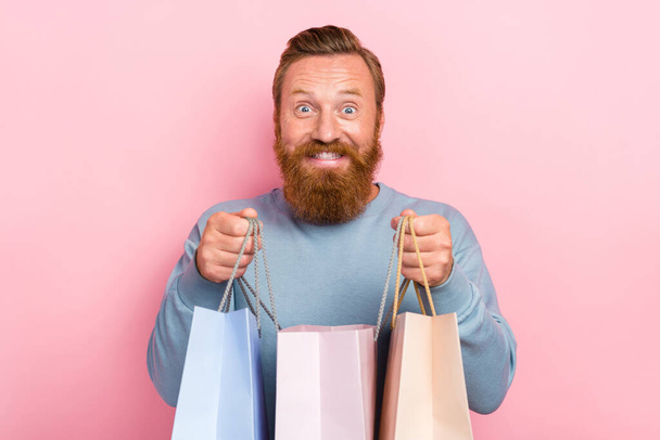 Portrait of ecstatic impressed man ginger beard dressed blue sweater satisfied holding shopping bags isolated on pink color background. - Fotó, kép