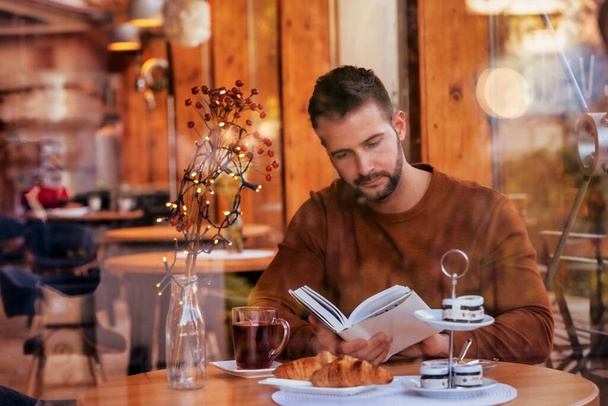 Portrait shot of handsome man sitting in cafe and reading a book. - Фото, изображение
