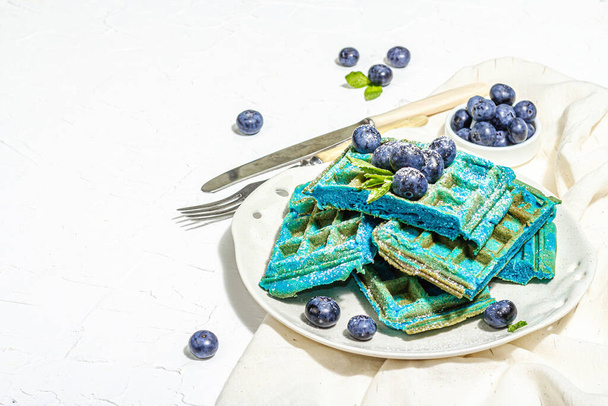 Hausgemachte belgische Waffeln mit Blaubeeren. Glutenfreies blaues Dessert, frisches Obst und Minze. Trendy hartes Licht, dunkler Schatten. Weißer Putzhintergrund, Kopierraum - Foto, Bild
