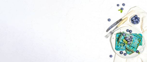 Gofres caseros de Bélgica con arándanos. Postre azul sin gluten, frutas frescas y menta. Luz dura de moda, sombra oscura. Fondo de yeso blanco, formato de banner - Foto, imagen