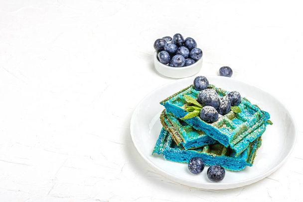 Hausgemachte belgische Waffeln mit Blaubeeren. Glutenfreies blaues Dessert, frisches Obst und Minze. Trendy hartes Licht, dunkler Schatten. Weißer Putzhintergrund, Kopierraum - Foto, Bild