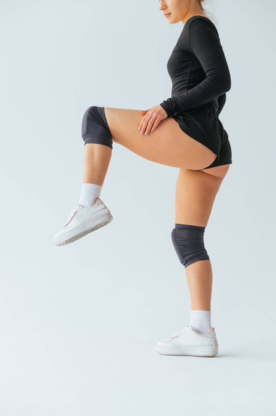 Athletic woman dancer in knee pads standing on one leg on a white background. Vertical - Фото, зображення