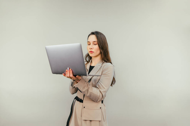 Concentrated attractive woman in suit working on laptop on beige wall background with serious face. Business woman with laptop isolated on a beige background. - Photo, Image