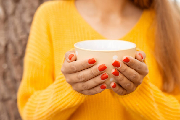 秋の森の中でお茶を飲んでいる女の子のクローズアップショット。涼しい秋の日にお茶を飲みながら手を暖める - 写真・画像