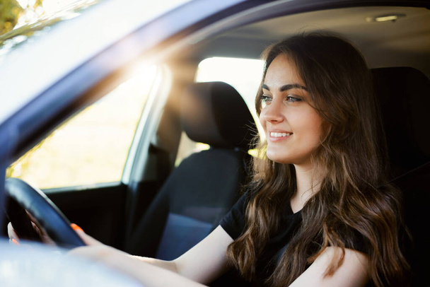 晴れた夏の日に車を運転する美しい若い現代の女の子。女性ドライバーだけで車の中で、クローズアップ、背景に太陽. - 写真・画像
