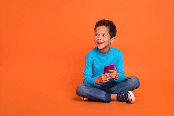 Full body photo of cute small boy hold gadget influencer look empty space dressed stylish blue outfit isolated on orange color background. - Foto, Bild