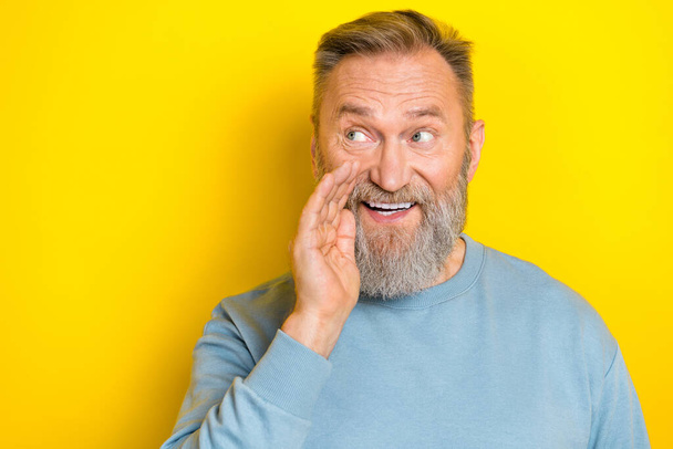 Photo of excited tricky cunning man pensioner dressed blue pullover arm mouth looking empty space isolated yellow color background. - Фото, изображение