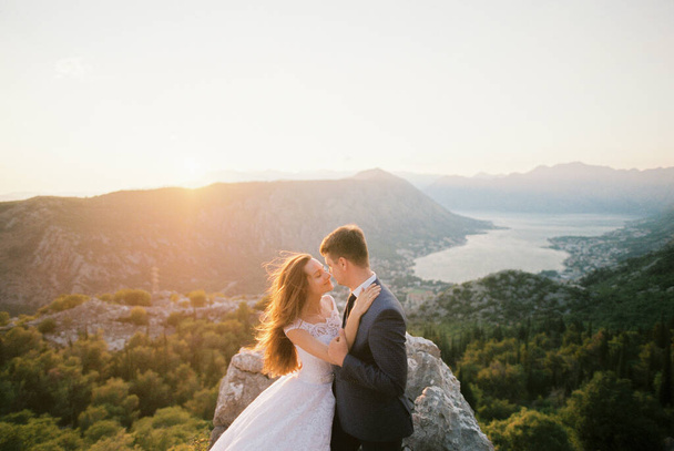 Novio abrazos novia de pie en la cima de la montaña por encima del valle. Kotor, Montenegro. Foto de alta calidad - Foto, Imagen