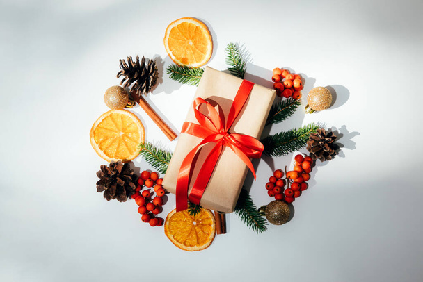 A gift wrapped in brown paper and tied red ribbon with a fir branch, a golden toy and a pine cone, orange on a white background. Flat lay - Zdjęcie, obraz