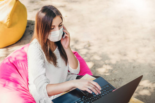 Kobieta menadżer freelancer siedzi przy stole na plaży z laptopem rozmawiającym przez telefon i szukającym pracy zdalnej podczas kwarantanny koronawirusu, pandemii, covid-19 - Zdjęcie, obraz