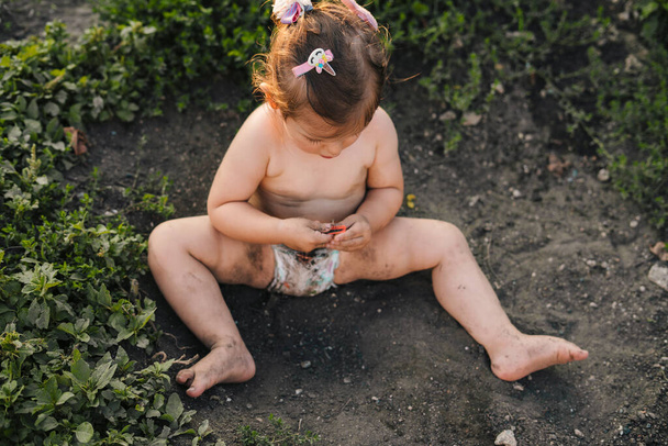 Curiosa bambina che gioca fuori in giardino, seduta a terra. Vista dall'alto. Giardino, infanzia, liberta '. Esplora il mondo che ti circonda. - Foto, immagini