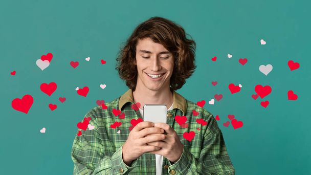 Online communication concept, collage. Funky millennial guy using smartphone on turquoise background, looking at gadget screen and cheerfully smiling, chatting with girlfriend, panorama - Photo, Image