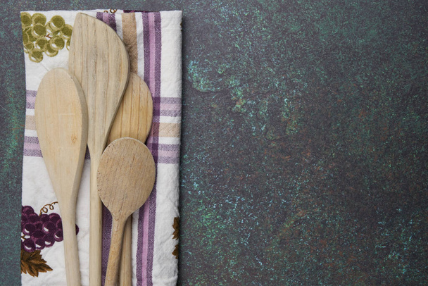 four wooden spoons with a green and purple plaid and grapes patterned kitchen towel on a blue green counter top - Photo, Image