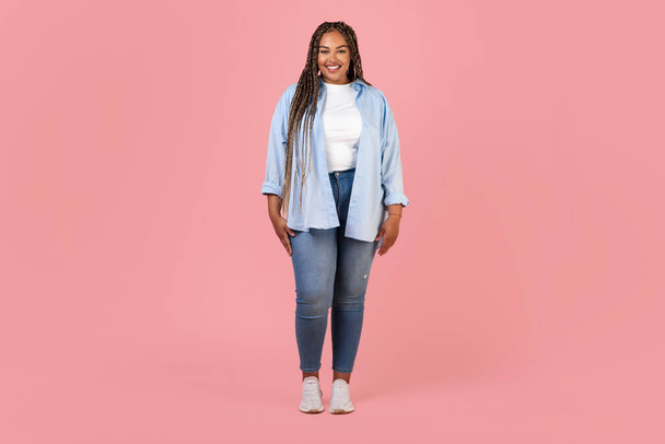 Full Length Shot Of Pretty Black Obese Lady Model Standing In Studio Over Pink Background, Smiling To Camera. Woman Posing Wearing Plus Size Clothes. Fashion And Style - Photo, Image