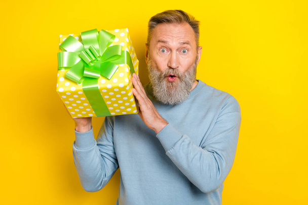 Portrait of impressed aged man arms hold giftbox pouted lips isolated on yellow color background. - Valokuva, kuva
