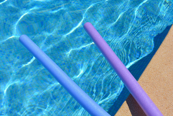 Letnie wibracje. Fioletowy i niebieski makaron pływacki pływający przy basenie - Zdjęcie, obraz