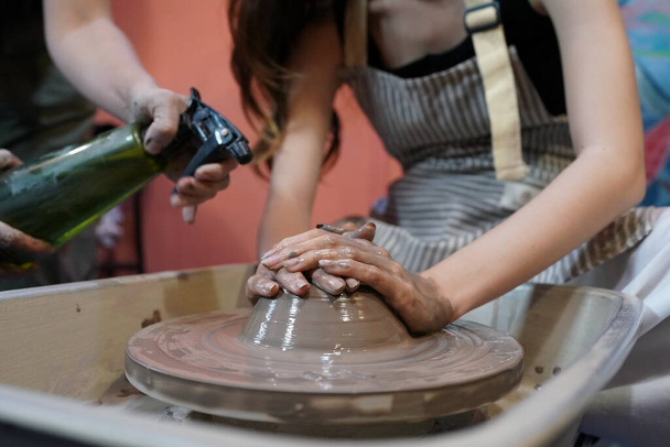Крупный план концентрированных красивых ремесленниц с гончарным кругом, работающих при формировании сосуда из мокрой глины - Фото, изображение