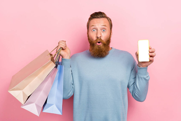 Photo of funny funky man with ginger hairdo dressed blue sweatshirt hold shopping bags smartphone isolated on pink color background. - Fotografie, Obrázek