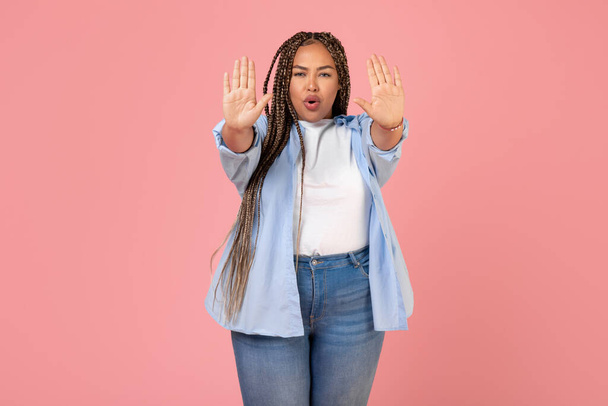 Odhodlaný africký Američan Plus velikost žena gesta stop s oběma rukama Zakazující něco, co hraje při pohledu na kameru stojící nad růžovým pozadím. Studio Shot - Fotografie, Obrázek