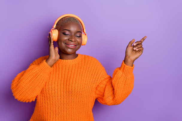 Foto de encantadora joven mujer disfrutar de auriculares melodía promo desgaste elegante caída naranja jersey de punto aislado sobre fondo de color púrpura. - Foto, imagen