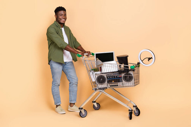 Photo of guy push cart have different items sell garage sale wear denim jeans isolated pastel color background. - Zdjęcie, obraz
