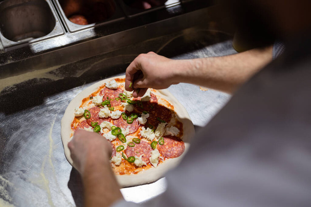 Pizza making process. Male chef hands making authentic pizza in the pizzeria kitchen. - Photo, Image
