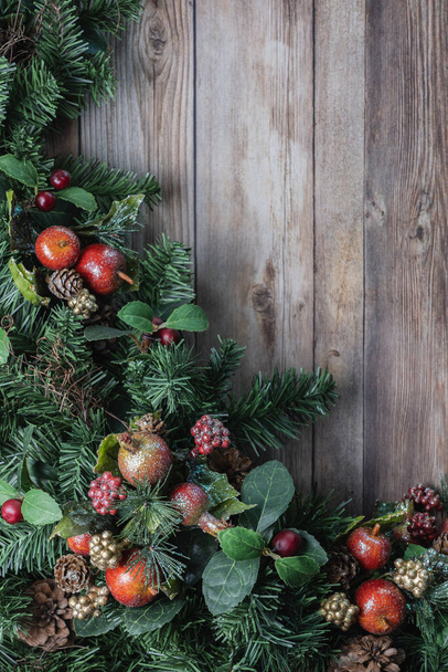 Kırmızı pırıltılı elma süslemeleri ve çam kozalakları Noel yeşilliği ve kırsal ahşap arka plan - Fotoğraf, Görsel