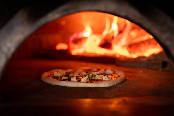 Pizza concept. Preparing traditional italian pizza. Long shovel for pizza, baking dough in a professional oven with open fire in interior of modern restaurant kitchen - Photo, Image