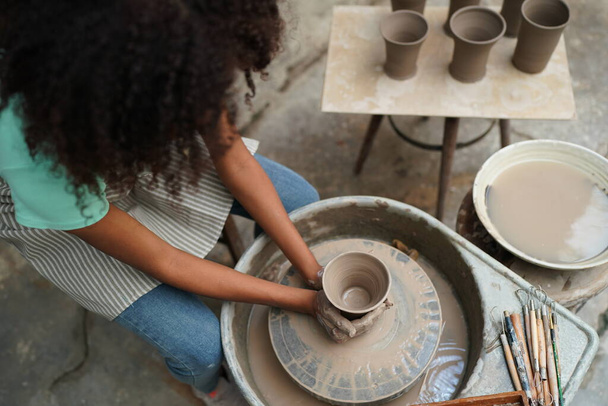 Молодая афро девушка ручной гончар, делающий глиняную вазу в керамической мастерской, владелец бизнеса.  - Фото, изображение