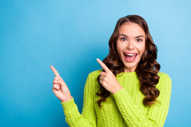 Photo of cute excited lady curly hairstyle point empty space dressed trendy autumn green knitted sweater isolated on blue color background. - Φωτογραφία, εικόνα