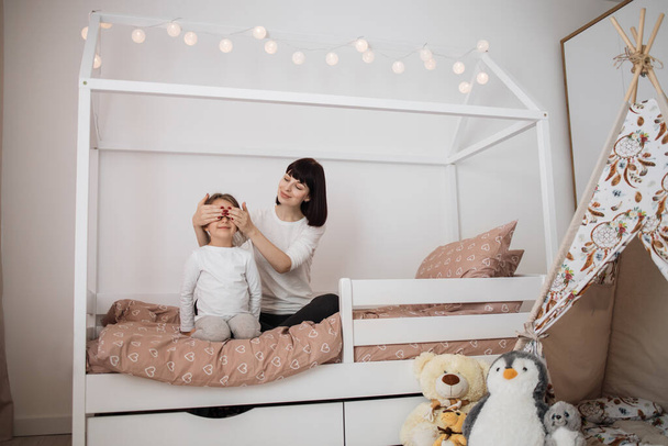 Cheerful mum babysitter closes eyes to her cute little preschool daughter. Happy carefree mother making surprise for her little child daughter laughing having fun feel joy at home. - Φωτογραφία, εικόνα