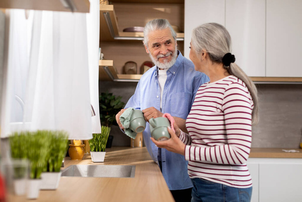 Smiling Senior Couple Making Domestic Chores Together, Wiping Cups In Kitchen, Happy Elderly Husband And Wife Cleaning Mugs At Home, Aged Spouses Enjoying Household Routine, Free Space - Фото, зображення