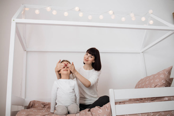 Cheerful mum babysitter closes eyes to her cute little preschool daughter. Happy carefree mother making surprise for her little child daughter laughing having fun feel joy at home. - Fotó, kép