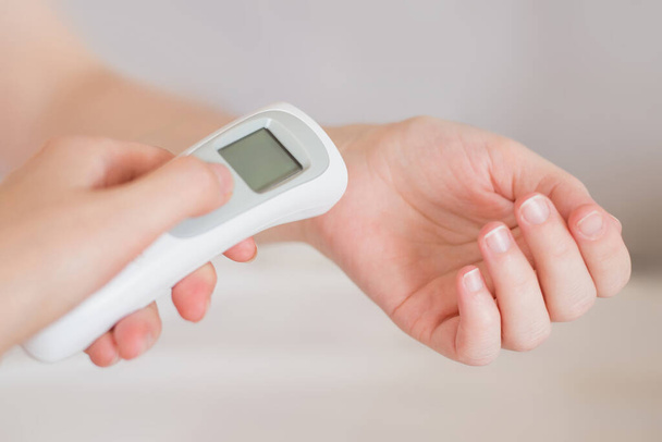 La mano de una mujer aplica un termómetro infrarrojo para medir la temperatura corporal. Fiebre alta con gripe y resfriados. Prevención del Coronavirus. Medición de la temperatura corporal en casa. Salud. Infección viral - Foto, imagen