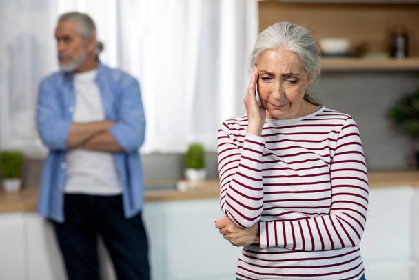 Πορτρέτο του αναστατωμένου ηλικιωμένου ζευγαριού που στέκεται στο εσωτερικό της κουζίνας μετά από καυγά, ανώτερος σύζυγος και σύζυγος που έχει εσωτερικές συγκρούσεις, που πάσχουν κρίση σχέσης, επιλεκτική εστίαση στο κλάμα γυναίκα - Φωτογραφία, εικόνα