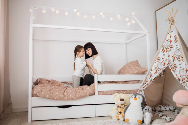 A nice girl and her mother hugging enjoying sunday morning. Good time at home. Child wakes up from sleep. Family playing on the bed in the bedroom. - Photo, image