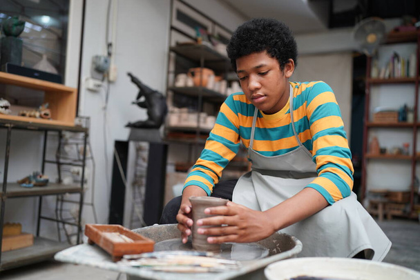 Νεαρός Αφρο έφηβος αγγειοπλάστη κατασκευή πήλινου αγγείου σε εργαστήριο κεραμικής - Φωτογραφία, εικόνα