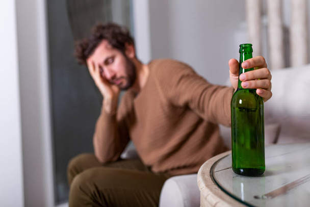 Alkoholista férfi benyúl egy üveg sörért, férfi egyedül iszik otthon. alkoholizmus, alkoholfüggőség és az emberek fogalma - férfi alkoholista egy üveg sörrel egyedül otthon - Fotó, kép