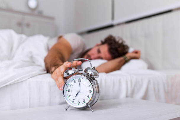 Man lying in bed turning off an alarm clock in the morning at 7am. Hand turns off the alarm clock waking up at morning, man turns off the alarm clock waking up in the morning from a call. - Photo, Image