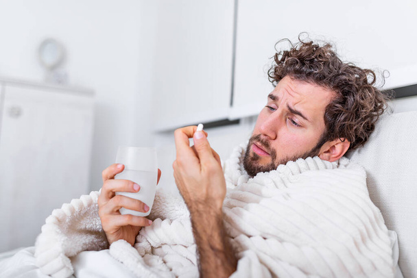 sick wasted man lying in bed wearing pajama suffering cold and winter flu virus having medicine tablets in health care concept Drinking pills with glass of water - Foto, Imagem