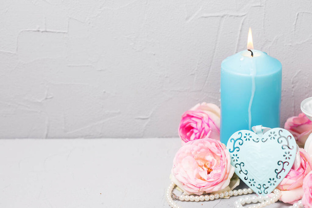 Romantic  still life background with blue heart,  blush roses and clematis flowers and  blue candle  on grey textured table.  Selective focus. Place for text.  - Foto, imagen
