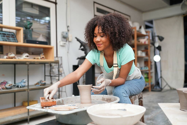 陶器の工房で粘土の花瓶を作る若いアフロの女の子の手の陶芸家、ビジネスオーナー.  - 写真・画像