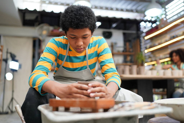 młody Afro nastolatek strony garncarz podejmowania wazon gliny w warsztacie garncarstwa - Zdjęcie, obraz