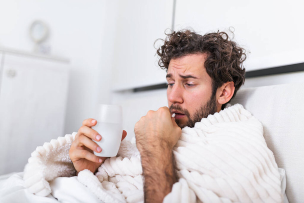 sick wasted man lying in bed wearing pajama suffering cold and winter flu virus having medicine tablets in health care concept Drinking pills with glass of water - Photo, Image