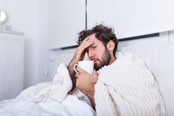 Людина хворіє, коли грип лежить у ліжку, перевіряючи температуру і п'ючи гарячий напій. Хворий чоловік лежить у ліжку з високою температурою. Холодний грип і мігрень
. - Фото, зображення