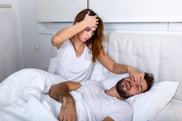 Couple in bed, man snoring and woman can't sleep. Snoring man and young woman. Couple sleeping in bed. Young girl can't sleep because of her man's snoring holding his nose. Snoring man problem - Photo, Image