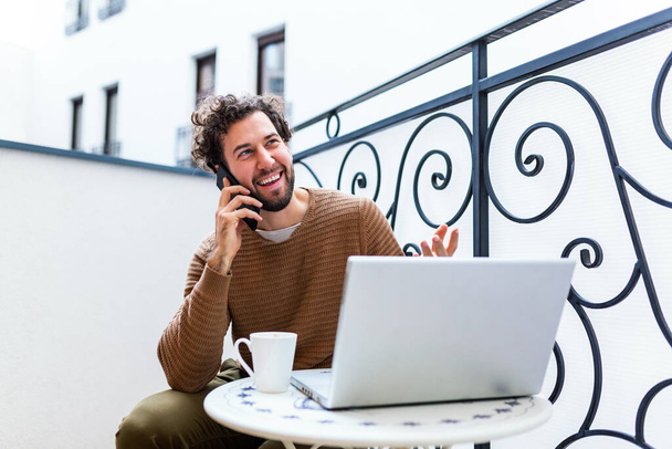 young man working from home using smart phone and notebook computer.Portrait of businessman talking on mobile phone and drinking coffee in the morning - Foto, afbeelding